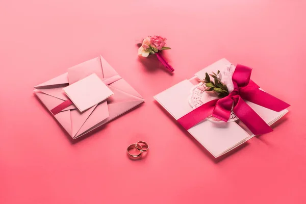 Wedding rings, boutonniere and pink envelopes with invitations on pink surface — Stock Photo