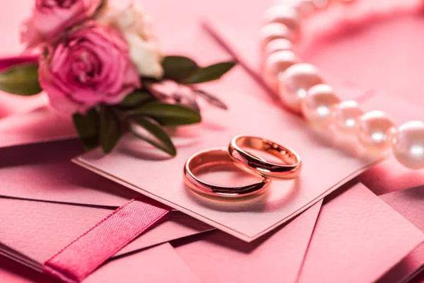 Wedding rings, pearl necklace and boutonniere on pink envelopes with invitations — Stock Photo