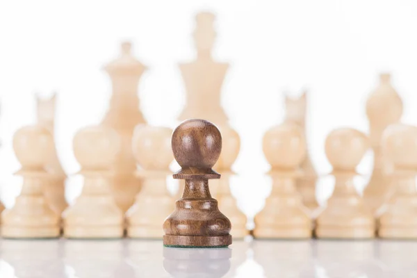 Черная шахматная пешка перед белыми фигурами на белом фоне — стоковое фото