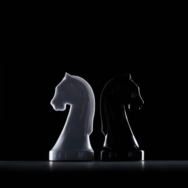 Siluetas de caballeros de ajedrez blancos y negros aislados en negro, concepto de negocio - foto de stock