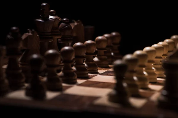 Figures d'échecs ordonnées sur l'échiquier isolé sur noir, concept d'affaires — Photo de stock