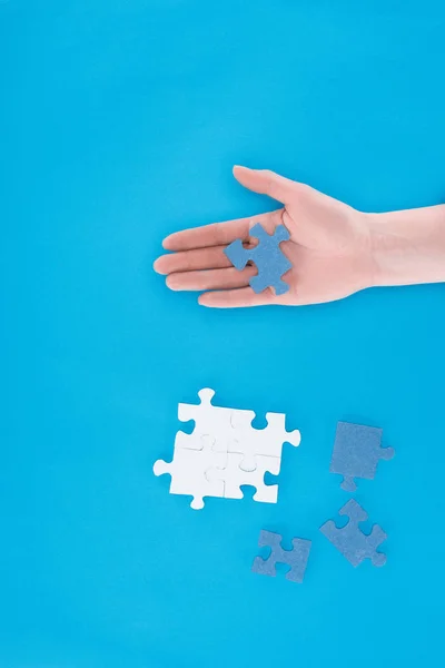 Imagem recortada de empresária montando quebra-cabeças e segurando uma peça na mão isolada em azul, conceito de negócio — Fotografia de Stock
