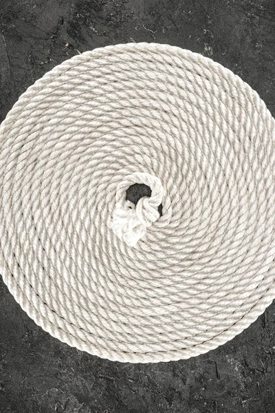 Vista superior de la cuerda náutica blanca dispuesta en círculo sobre una mesa de hormigón oscuro - foto de stock