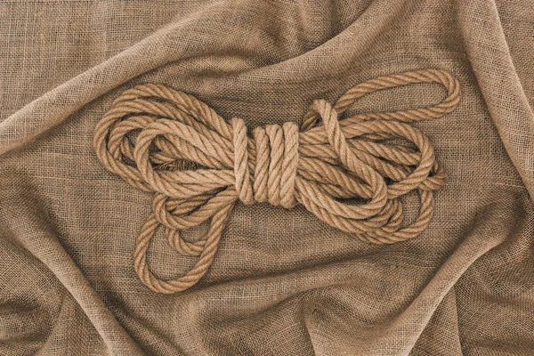 Vista superior de cuerda náutica marrón atada arreglada sobre tela de saco - foto de stock