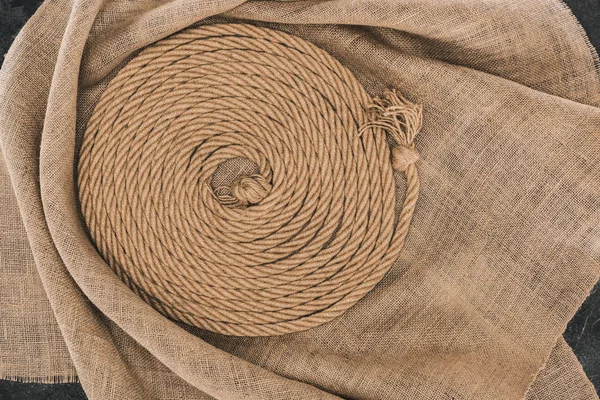 Draufsicht auf braunes nautisches Seil, kreisförmig auf Sacktuch auf dunkler Betonoberfläche angeordnet — Stockfoto