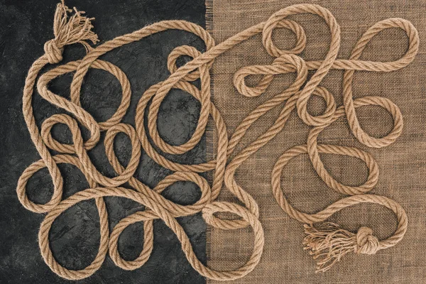 Flat lay with brown marine ropes with knots on sackcloth and dark concrete surface — Stock Photo