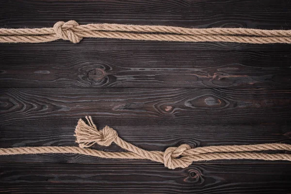 Vista superior de arranjo de cordas náuticas marrons com nós em mesa de madeira escura — Fotografia de Stock