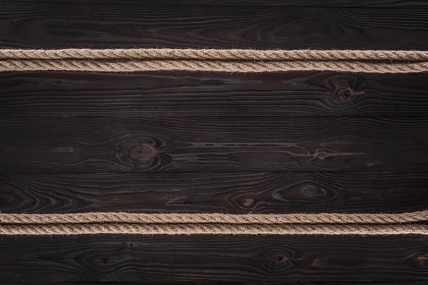 Vista superior de disposición de cuerdas náuticas marrones sobre mesa de madera oscura - foto de stock