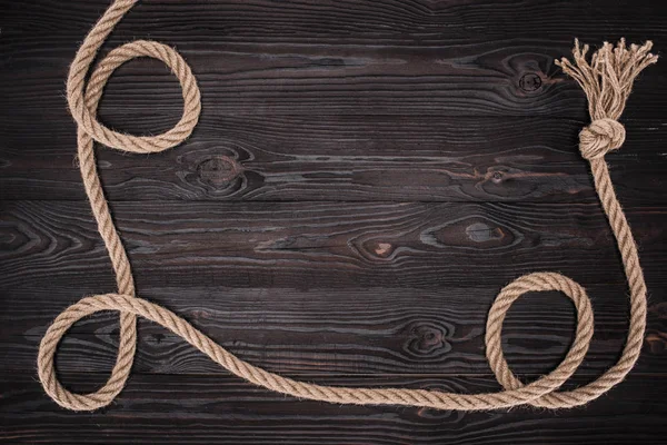 Top view of brown nautical rope with knot on dark wooden surface — Stock Photo