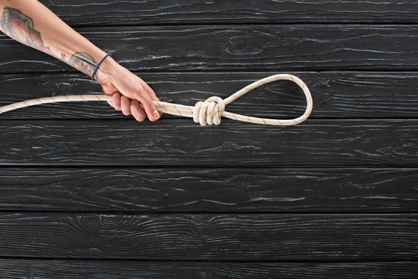 Partial view of female hand with marine rope with knot on dark wooden surface — Stock Photo