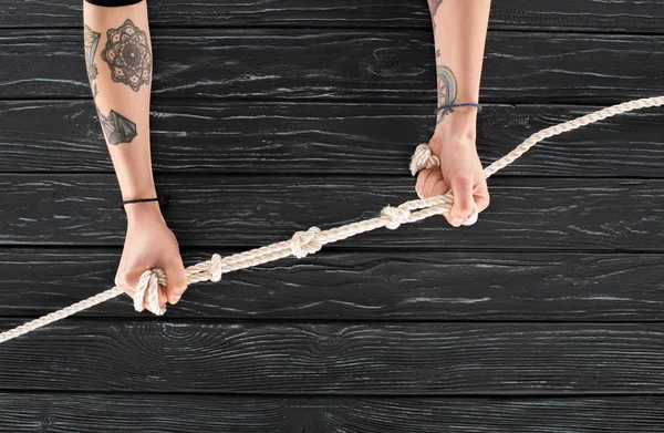 Partial view of woman holding marine rope with knots on dark wooden surface — Stock Photo