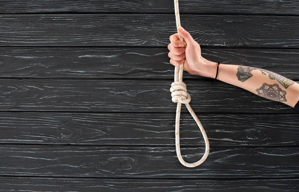 Partial view of female hand with marine rope with knot on dark wooden surface — Stock Photo