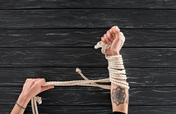 Partial view of female hands with rope around on dark wooden tabletop — Stock Photo