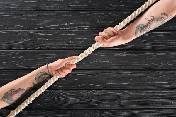 Cropped shot of people pulling marine rope on dark wooden surface — Stock Photo