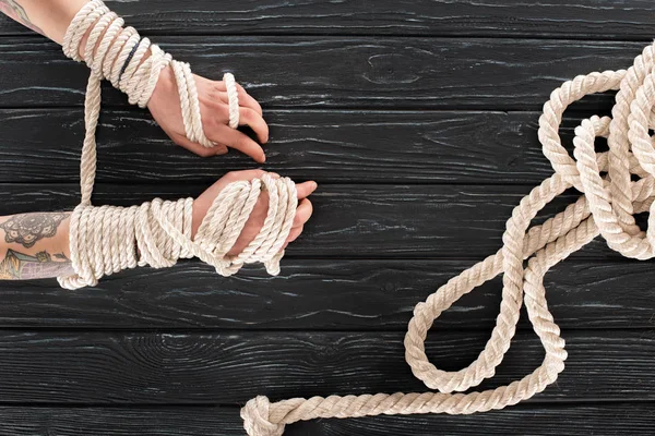 Cropped shot of female tattooed hands tied in rope on dark wooden tabletop — Stock Photo