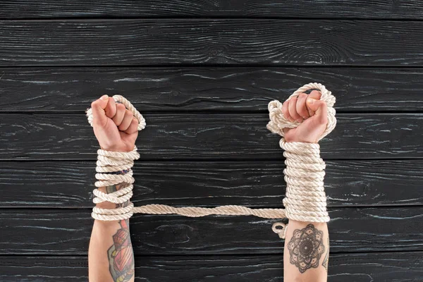 Cropped shot of female tattooed hands tied in rope on dark wooden tabletop — Stock Photo