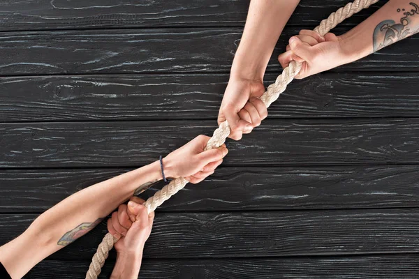 Cropped shot of people pulling marine rope on dark wooden surface — Stock Photo