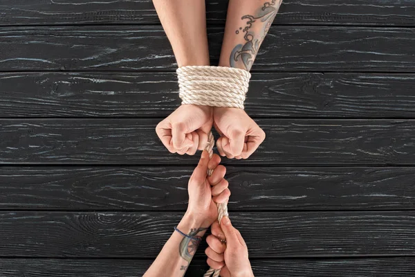 Partial view of woman tying rope around males hands on dark wooden surface — Stock Photo