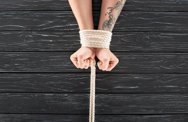 Cropped shot of male hands tied with marine rope on dark wooden surface — Stock Photo