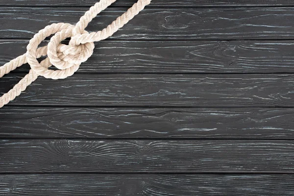 Top view of white nautical rope with knot on dark wooden surface — Stock Photo