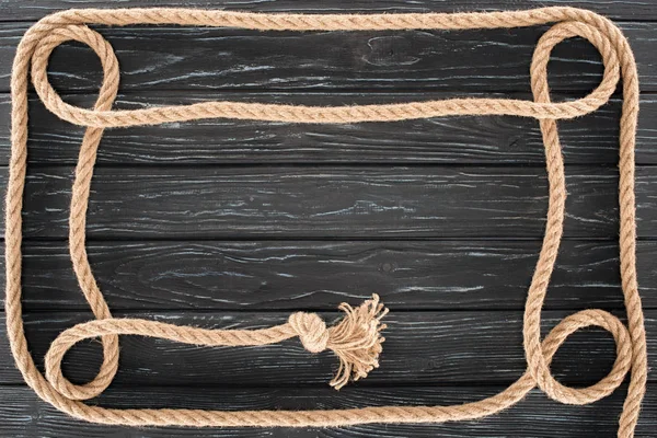 Top view of brown rope with knot on dark wooden surface — Stock Photo