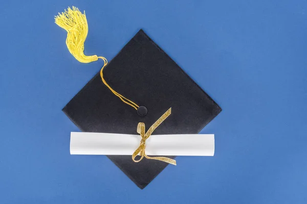 Concetto di laurea con diploma e tappo di laurea isolato su blu — Foto stock