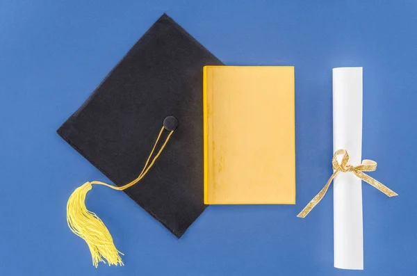 Abschlussmütze mit Diplom und Buch isoliert auf blau — Stockfoto