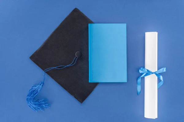 Concetto di scuola superiore con diploma e tappo di laurea isolato su blu — Foto stock