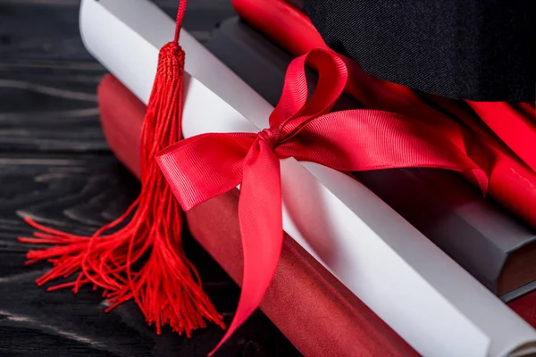 Graduation hat and diploma with red ribbon on stack of books — Stock Photo