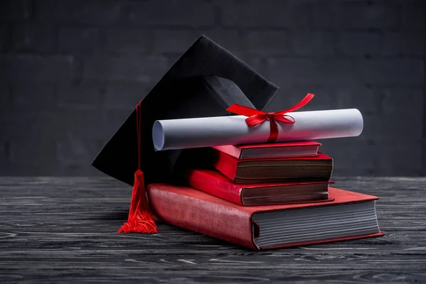 Montón de libros con diploma y sombrero de graduación en la mesa - foto de stock