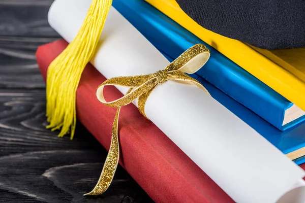 Graduation hat and diploma with yellow ribbon  on stack of books — Stock Photo