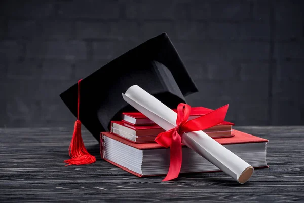 Livros empilhados com diploma e chapéu de graduação na mesa — Stock Photo