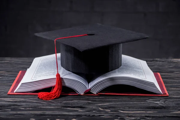 Offenes Buch mit Graduiertenmütze auf Holztisch — Stockfoto