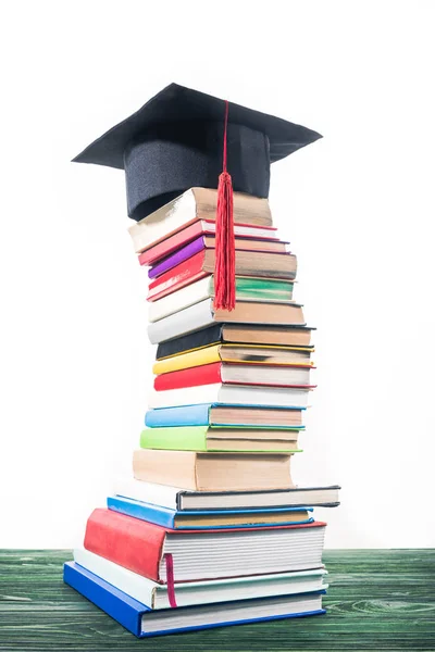 Graduation cap on bent tower of stacked books — Stock Photo