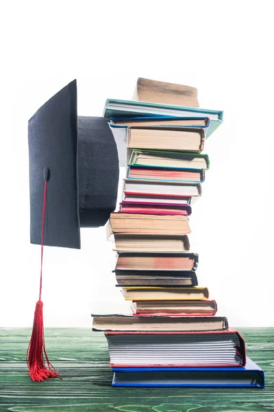 Boné de graduação fixado entre livros empilhados — Fotografia de Stock