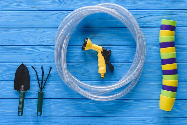 Top view of stack of colorful flowers pots, gardening tools and hose on blue wooden planks — Stock Photo