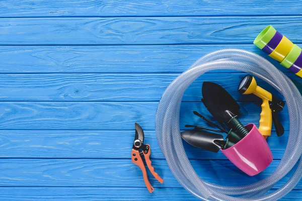 Vista superior de macetas, mangueras y herramientas de jardinería en tablones de madera azul - foto de stock