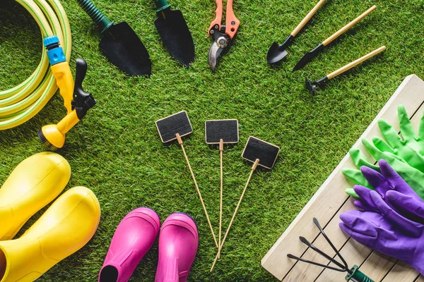 Vue de dessus des tableaux noirs vides entourés de bottes en caoutchouc, de matériel de jardinage et de gants de protection sur herbe — Photo de stock