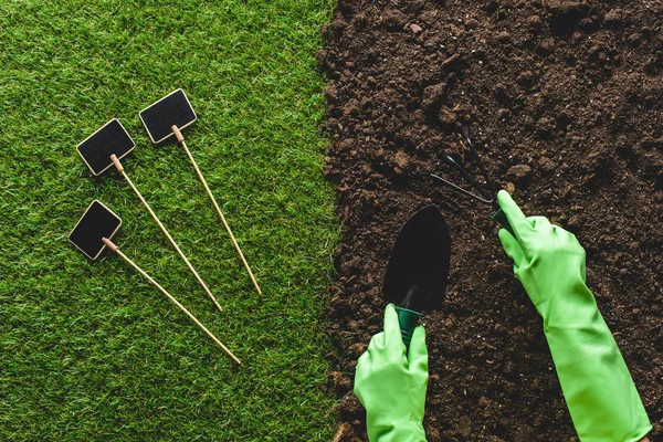 Обрезанное изображение садовника в защитных перчатках, работающего с садовыми инструментами и пустыми досками на траве — стоковое фото