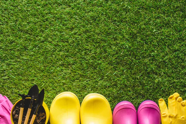 Vista superior de botas de goma, guantes protectores y maceta con herramientas de jardinería - foto de stock