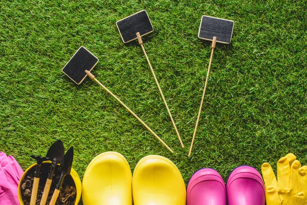 Vista superior de pizarras vacías, botas de goma, guantes protectores, maceta de flores y herramientas de jardinería - foto de stock