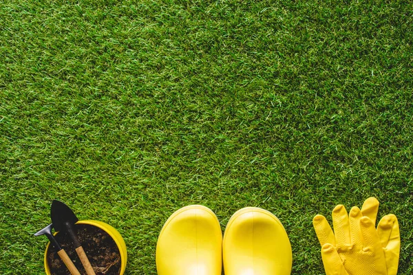 Vista superior de botas de goma amarillas, guantes protectores y maceta con herramientas de jardinería - foto de stock
