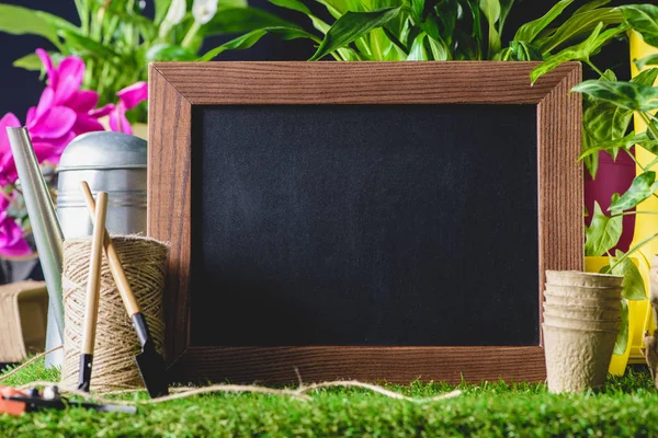 Closeup shot of empty blackboard and gardening equipment on lawn — Stock Photo