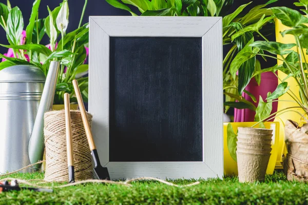 Closeup shot of empty blackboard and gardening equipment on lawn — Stock Photo