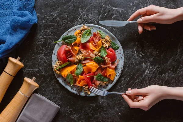 Vista superior parcial de la persona comiendo deliciosa ensalada con mejillones, verduras y jamón - foto de stock