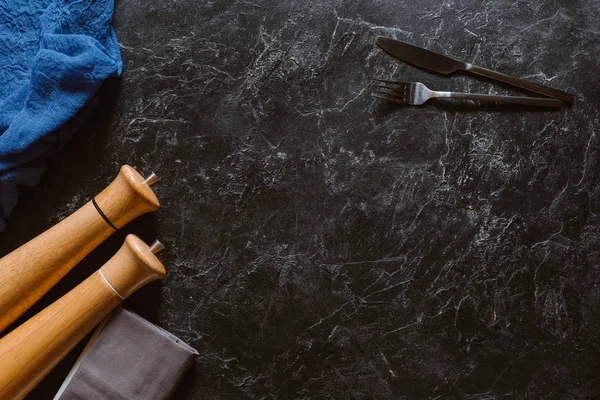 Top view of wooden containers with seasonings, fork and knife on black marble surface — Stock Photo