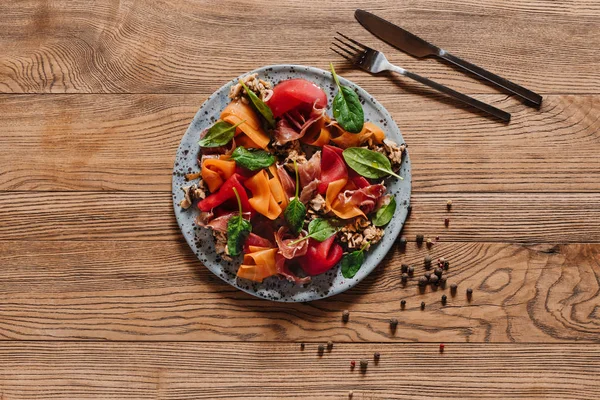 Salad with mussels, vegetables and jamon, fork with knife and peppercorns on wooden table — Stock Photo