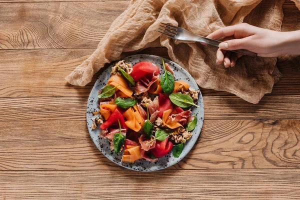 Cropped shot of human hand holding fork and salad with mussels, vegetables and jamon on wooden table — Stock Photo