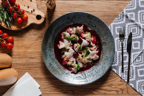 Вид сверху на вкусный севиче с дорадо в тарелке, вилкой с ножом и свежими помидорами на деревянном столе — стоковое фото