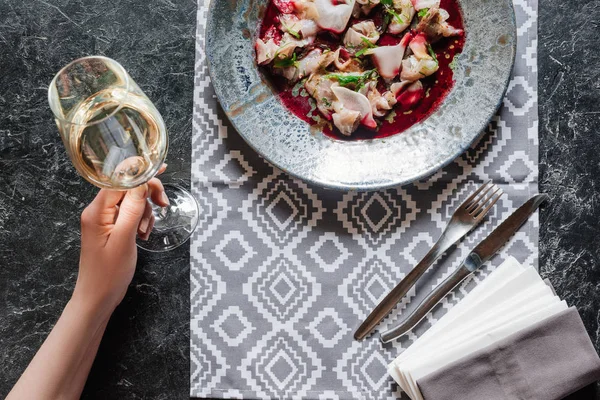 Recortado tiro de persona sosteniendo vaso de vino y comiendo ceviche gourmet con dorado - foto de stock